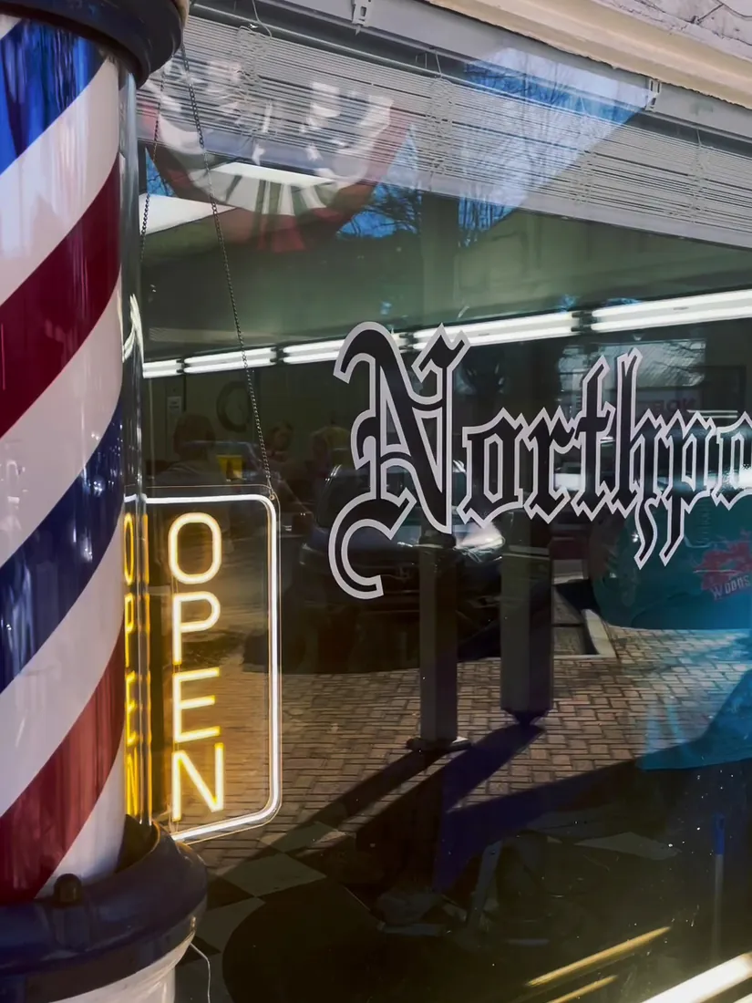 Close-up of the red, white and blue barber pole beside a glowing neon OPEN sign, with Northport lettered on the shop window